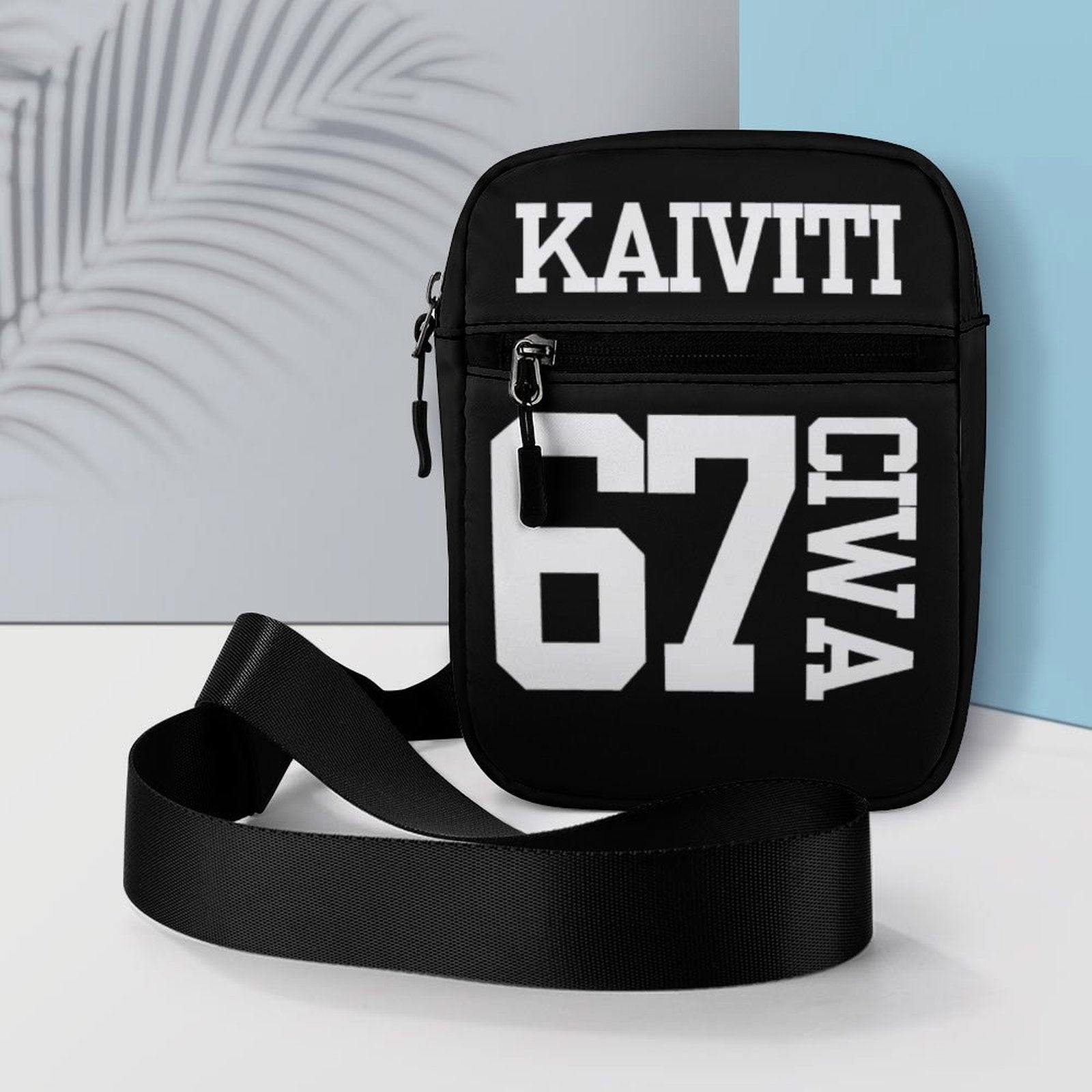 Black crossbody bag with 'KAIVITI 67 CIWA' text on a light gray and blue background